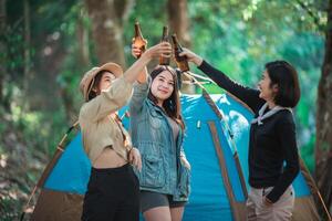 mulheres jovens torcem e bebem bebidas na frente da barraca de acampamento foto
