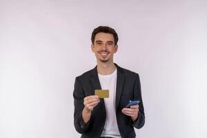 retrato do feliz jovem homem de negocios em pé usando Móvel célula telefone e segurando crédito banco cartão isolado em branco cor fundo estúdio foto