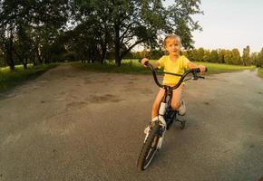 pequeno menina com equitação bicicleta às pôr do sol foto