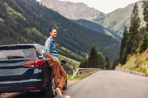 bonito jovem homem em pé ao ar livre perto dele carro e . jovem homem em estrada viagem foto