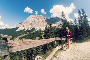 traseiro Visão do uma fêmea caminhante caminhando em uma trilha dentro a Alpes perto Ehrwald, Tirol, Áustria. panorama com grama, árvores, rochoso montanhas e azul céu. foto