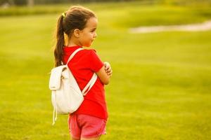 pequeno menina com uma mochila indo para escola. costas Visão foto