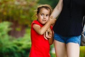 fechar acima do infeliz Sombrio esfolado criança pequena bebê menina chorando enquanto dela irreconhecível mãe segurando dela em mãos. foto