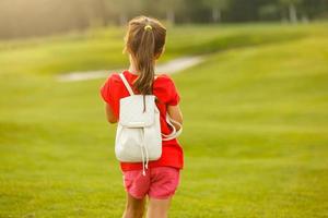 pequeno menina com uma mochila indo para escola. costas Visão foto