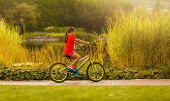 criança equitação bicicleta. criança bicicleta dentro ensolarado parque. pequeno menina desfrutando bicicleta passeio em dela caminho para escola caloroso verão dia. pré-escolar Aprendendo para Saldo bicicleta esporte para crianças. foto