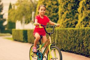 criança equitação bicicleta. criança em bicicleta dentro ensolarado parque. pequeno menina desfrutando bicicleta passeio dela caminho para escola caloroso verão dia. pré-escolar Aprendendo para Saldo bicicleta esporte para crianças. foto