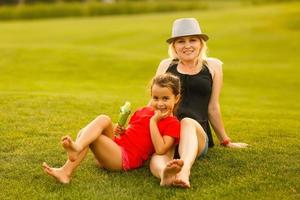 mãe e filha sentado juntos em verde grama. mãe e filha tendo engraçado conversação. foto