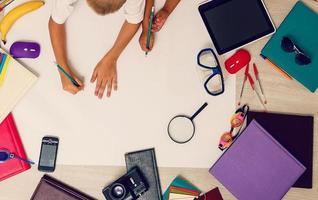 beleza pré-escolar menina dentro branco e Preto uniforme diligentemente escrevendo dentro caderno, perto - vermelho maçã, muitos colorida livros e lápis, topo Visão foto