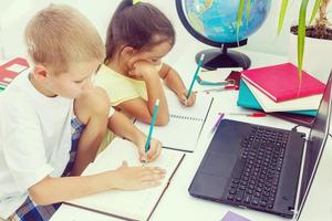 retrato do dois escolares sentado de 1 escrivaninha durante desenhando lição enquanto Garoto olhando às dele companheiros caderno foto