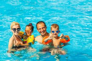 feliz família com dois crianças tendo Diversão dentro a natação piscina. verão período de férias conceito foto
