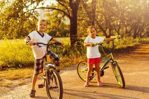 dois crianças empurrando bicicletas ao longo país rastrear foto