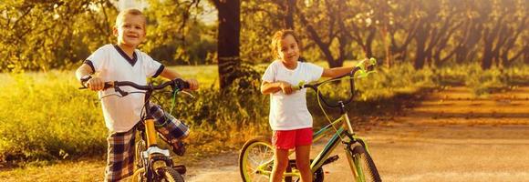 dois crianças empurrando bicicletas ao longo país rastrear foto