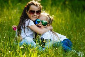 dois pequeno meninas em pé juntos dentro a parque, 1 abraços outro foto