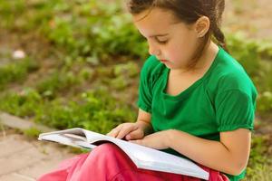 Lille menina retrato com livros dentro jardim durante auto Educação às lar. distante controlo remoto auto aprendizado. moderno escola família estudar. foto