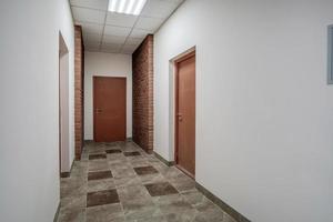 branco esvaziar grandes corredor com vermelho tijolo paredes e portas dentro interior do moderno apartamentos ou escritório foto