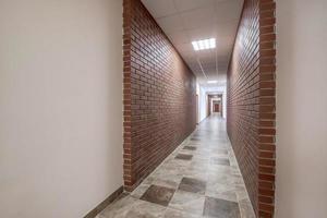 branco esvaziar grandes corredor com vermelho tijolo paredes e portas dentro interior do moderno apartamentos ou escritório foto