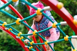 retrato do feliz pequeno loiro menina jogando em uma corda rede Parque infantil ao ar livre foto