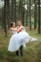 jovem casal noiva dentro uma branco curto vestir e noivo dentro uma cinzento terno dentro uma pinho floresta foto