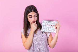 jovem lindo mulher segurando menstruação calendário sobre isolado fundo com surpresa face. jovem menina segurando menstruação calendário com confuso face, receoso e animado com medo expressão foto