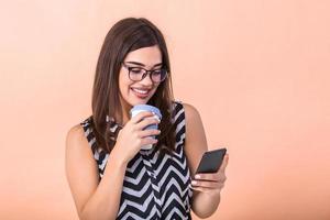jovem inteligente bem sucedido mulher dentro óculos tendo quebrar, segurando café para ir e surfar a Internet com dela Móvel inteligente telefone foto