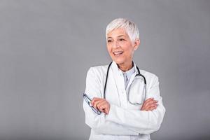 retrato do Senior fêmea médico com estetoscópio braço Cruz isolado em fundo. a médico em pé com alegre gesticulando. ela vestindo médico uniforme dentro hospital. saúde seguro conceito. foto