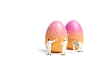 pessoas em miniatura pintando ovos de páscoa para o dia de páscoa em um fundo branco foto