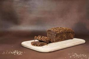 lado Visão em Preto pão com cereais fatiado em uma de madeira corte borda contra uma Castanho fundo. foto