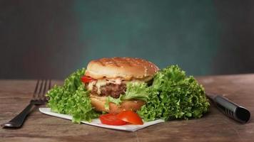 uma saboroso hamburguer mentiras em uma de madeira mesa contra uma verde fundo. uma faca e uma garfo mentira em a mesa foto