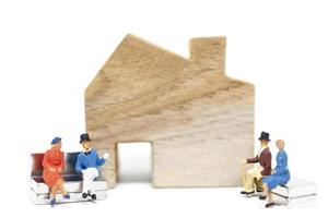 marido e mulher em miniatura sentados em frente a uma casa em um fundo branco, conceito de família foto
