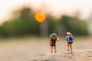 viajantes em miniatura com mochilas caminhando sobre uma rocha, conceito de viagem e aventura