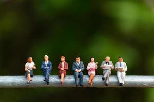 Empresários em miniatura sentados em um fio com um fundo verde, conceito de equipe de negócios foto