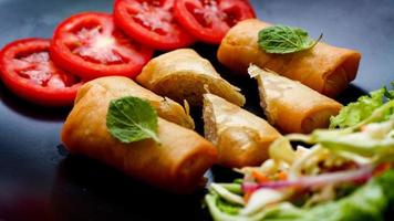 frito Primavera rolos com legumes e tomates colocada dentro uma Preto prato em uma Preto de madeira mesa e mergulho molho. foto