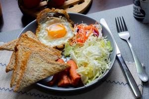 café da manhã, frito ovos, frito salsicha, vegetal salada e torrada em uma Castanho de madeira mesa com café. foto