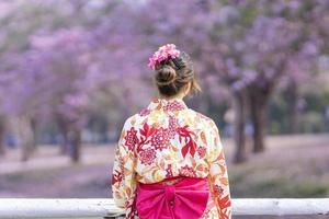a costas do japonês mulher dentro tradicional quimono vestir é olhando às a Visão do sakura flor árvore dentro a parque às cereja Flor Primavera festival com cópia de espaço foto