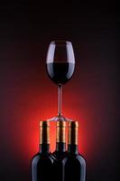 garrafas de vinho e copo cheio com fundo vermelho e preto foto