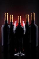 garrafas de vinho e copo cheio com fundo vermelho e preto foto