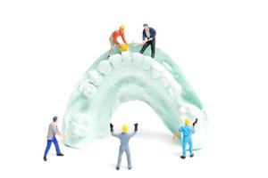trabalhadores em miniatura obtendo dentes falsos e colocando-os em uma dentadura feita com gesso, conceito de laboratório de prótese dentária foto