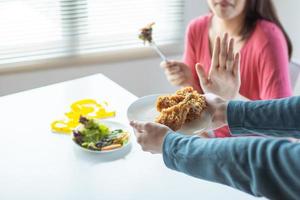 mulher comendo uma salada afastando as mãos segurando um prato de frango frito em uma mesa de jantar ao lado de uma janela foto