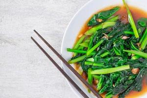 Couve chinesa frita com molho de ostra com pauzinhos em um prato branco na mesa de madeira foto