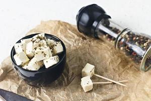 queijo feta marinado em um prato sobre uma placa de madeira com especiarias em um fundo branco foto