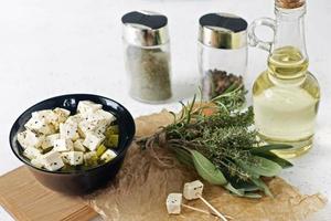 queijo feta marinado em um prato sobre uma placa de madeira com especiarias em um fundo branco foto