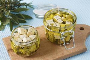 queijo feta marinado em uma jarra de vidro e especiarias contra um fundo azul foto