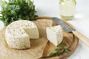 queijo branco em uma placa de madeira em um fundo branco com verduras foto