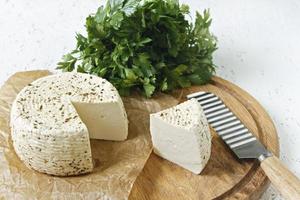 queijo branco em uma placa de madeira em um fundo branco com verduras foto