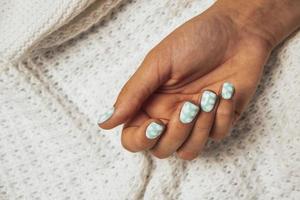 uma lindo fêmea mão com uma colori manicure em a fundo do uma de lã branco tricotado xadrez foto