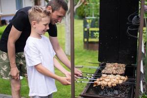 alegre Papai e filho assado carne em a grade foto