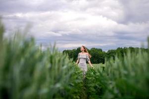 uma fofa menina com grandes cabelo dentro uma vestir corre através uma trigo campo foto