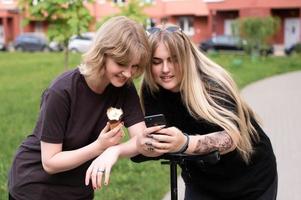 dois engraçado meninas estão sentado em uma balanço dentro a cidade e levando selfies em seus telefone. adolescentes sorrir foto