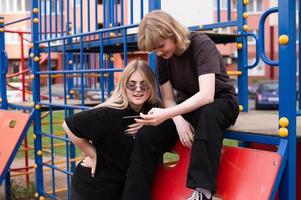 dois Adolescência meninas estão sentado em a Parque infantil com uma telefone foto