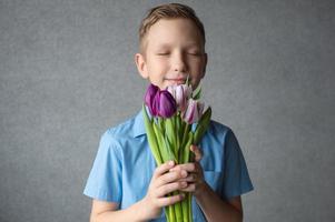 uma fofa Garoto é segurando uma colorida ramalhete do tulipas dentro dele mãos. cheiro roxa tulipas foto